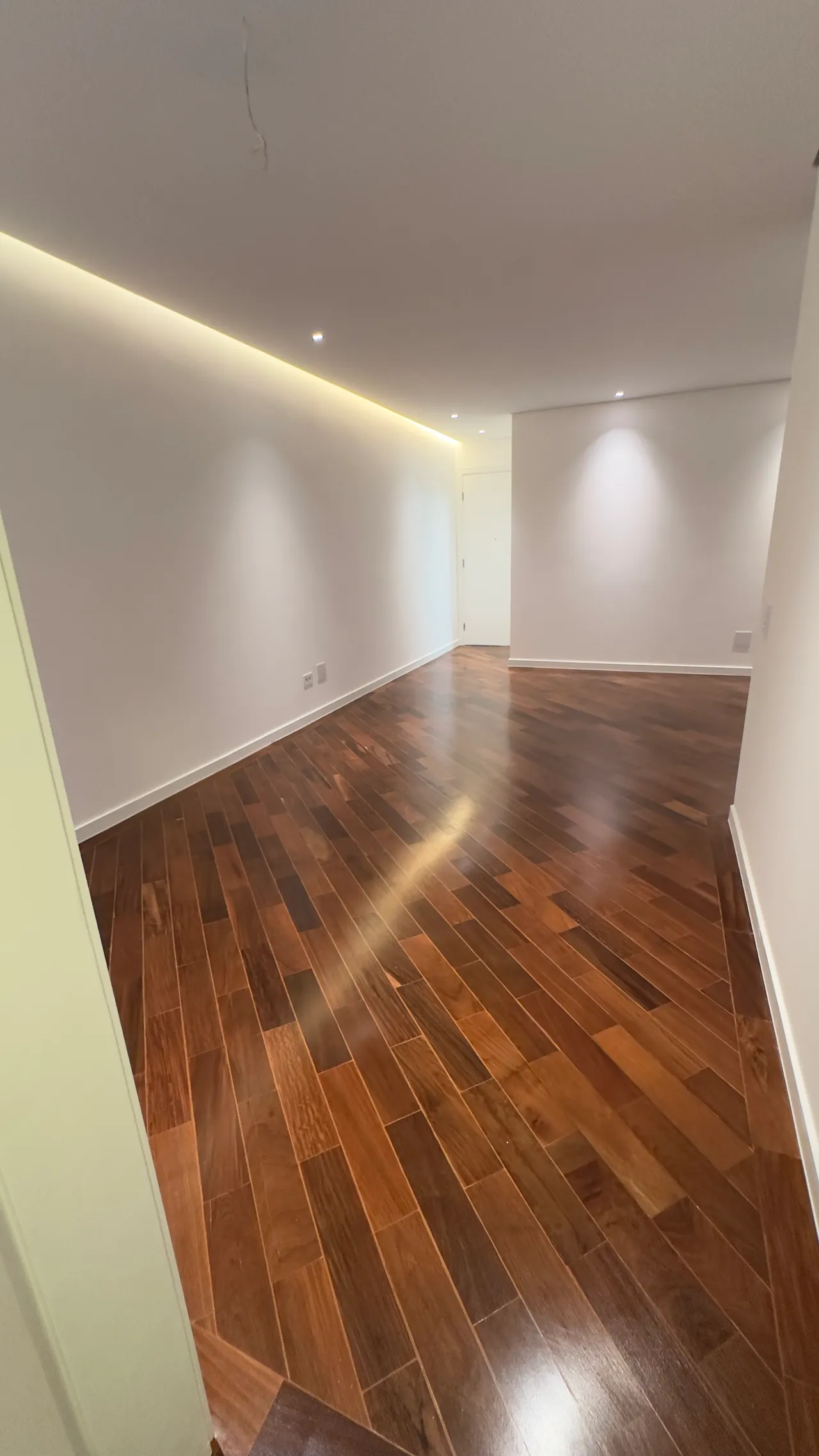 Sala ampla com piso de madeira e sanca de luz indireta